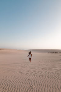 Man on sand dune in desert against clear sky