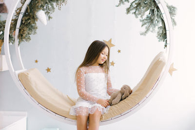 Cute girl holding a soft favorite toy and sitting on a swing decorated for christmas