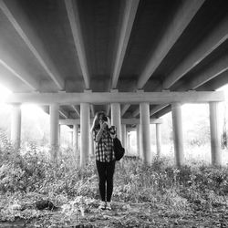 Woman photographing through camera while standing below bridge