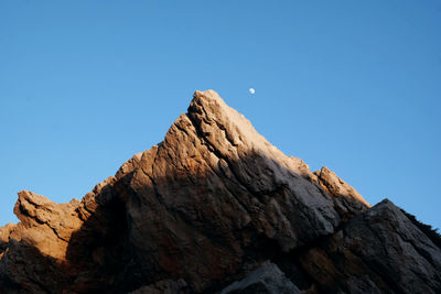 Low angle view of rocky mountains against clear blue sky