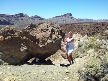 Full length of young woman standing on rock against sky