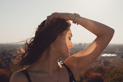 Beautiful woman with hand in hair standing against clear sky during sunny day