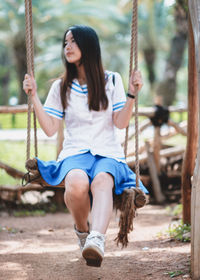 Full length of woman sitting on swing at playground