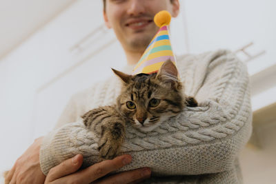 A young guy is holding a cat with a hat in his hands.