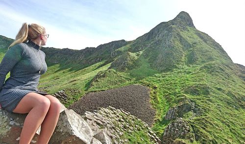 Woman sitting on rock against sky