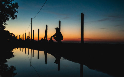 Silhouette men by lake against sky during sunset