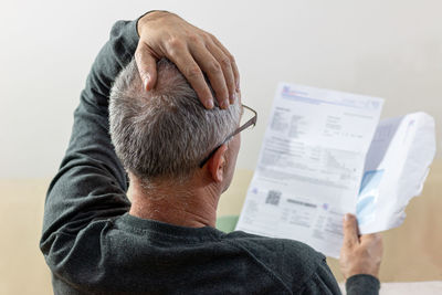 Middle-aged man going through bills, reading shocking unexpected news in paper document.