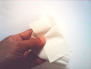 Close-up of hand holding paper against white wall