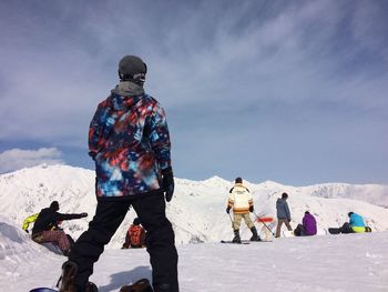 People at snow covered field by mountains against sky