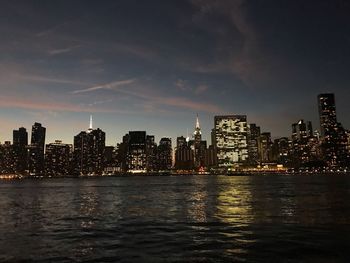 Illuminated buildings by sea against sky at night