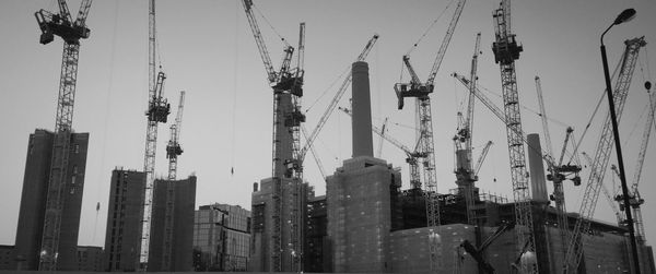 Low angle view of cranes and buildings against sky