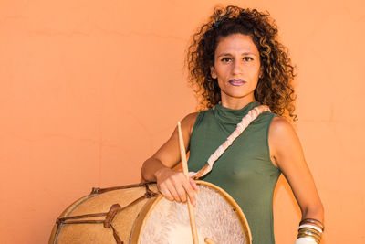 Portrait of woman carrying drum while standing against wall