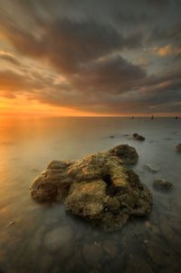 Rocks by sea against sky during sunset