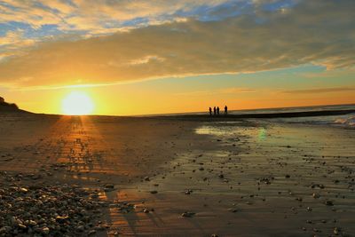 Scenic view of beach against cloudy sky during sunset