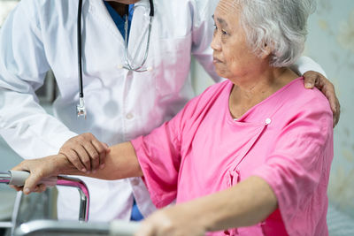 Midsection of doctor assisting senior woman in walking