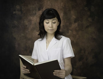 Young woman reading book against wall