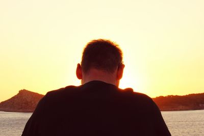 Rear view of man in front of sea against sky during sunset