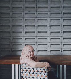 Portrait of young woman sitting on chair against wall