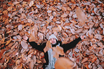 High angle view of woman with arms outstretched lying on dry leaves on field