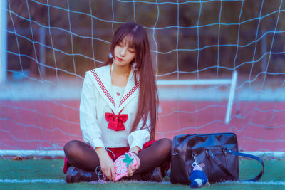 Young woman listening to music while sitting against net on soccer field