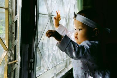 Cute baby girl looking through window at home 