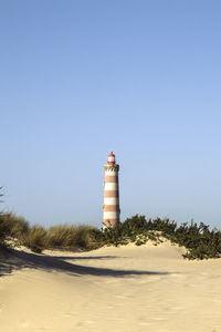 Lighthouse on beach against clear sky