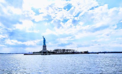 Statue by sea against cloudy sky