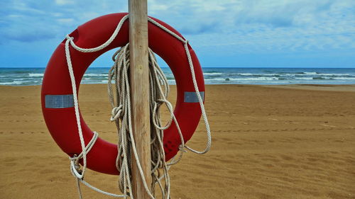 Red flag on wooden post at beach against sky