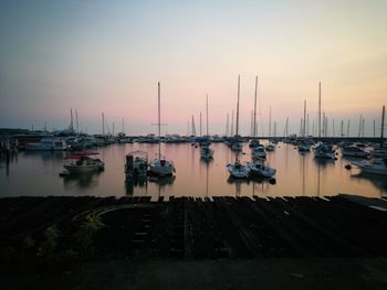 Boats moored in harbor at sunset