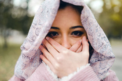 Close-up portrait of teenage girl with mouth covered by hands