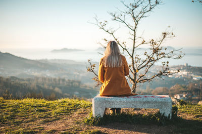 Rear view of woman sitting on bench against sky