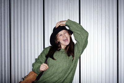 Cheerful young woman wearing hat in front of corrugated wall