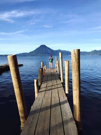 Rear view of young woman standing on pier over sea against sky