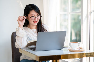 Young woman using mobile phone while sitting on table