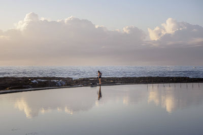 Distance view of person standing at sea shore against sky