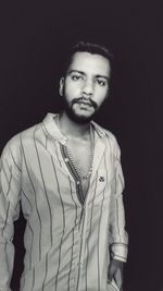 Portrait of young man standing against black background