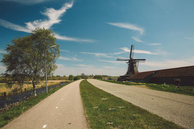 Road by traditional windmill against sky