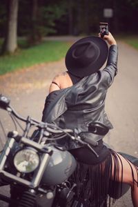 Rear view of man photographing woman riding motorcycle