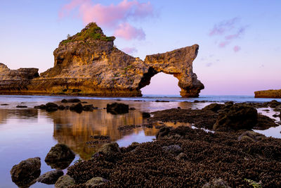 Rock formation on beach against sky during sunset