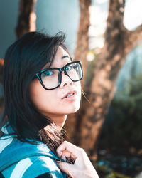 Portrait of woman wearing eyeglasses sitting against tree