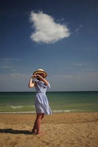 Woman making heart shape while standing at beach against sea and sky