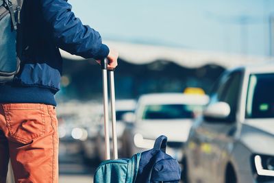 Midsection of man standing with luggage by cars on street