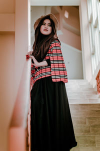 Low angle view of young woman looking away while standing on steps at home