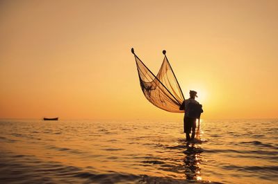 Man fishing in sea at sunset