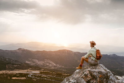 Rear view of woman sitting on rock against sky