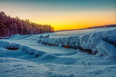 Snow covered landscape against sky during sunset