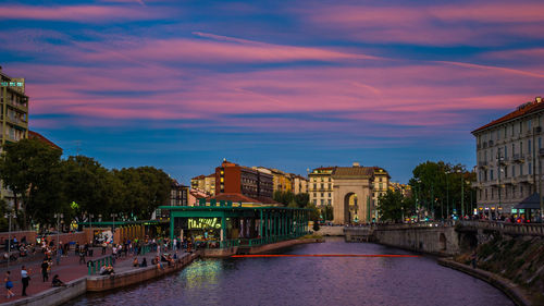 Canal amidst buildings in city against sky at sunset