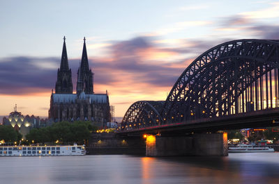 Illuminated bridge over river against sky at sunset