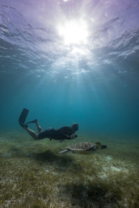Free diver swimming underwater with turtle in ocean