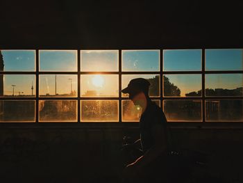 Woman looking through window at sunset